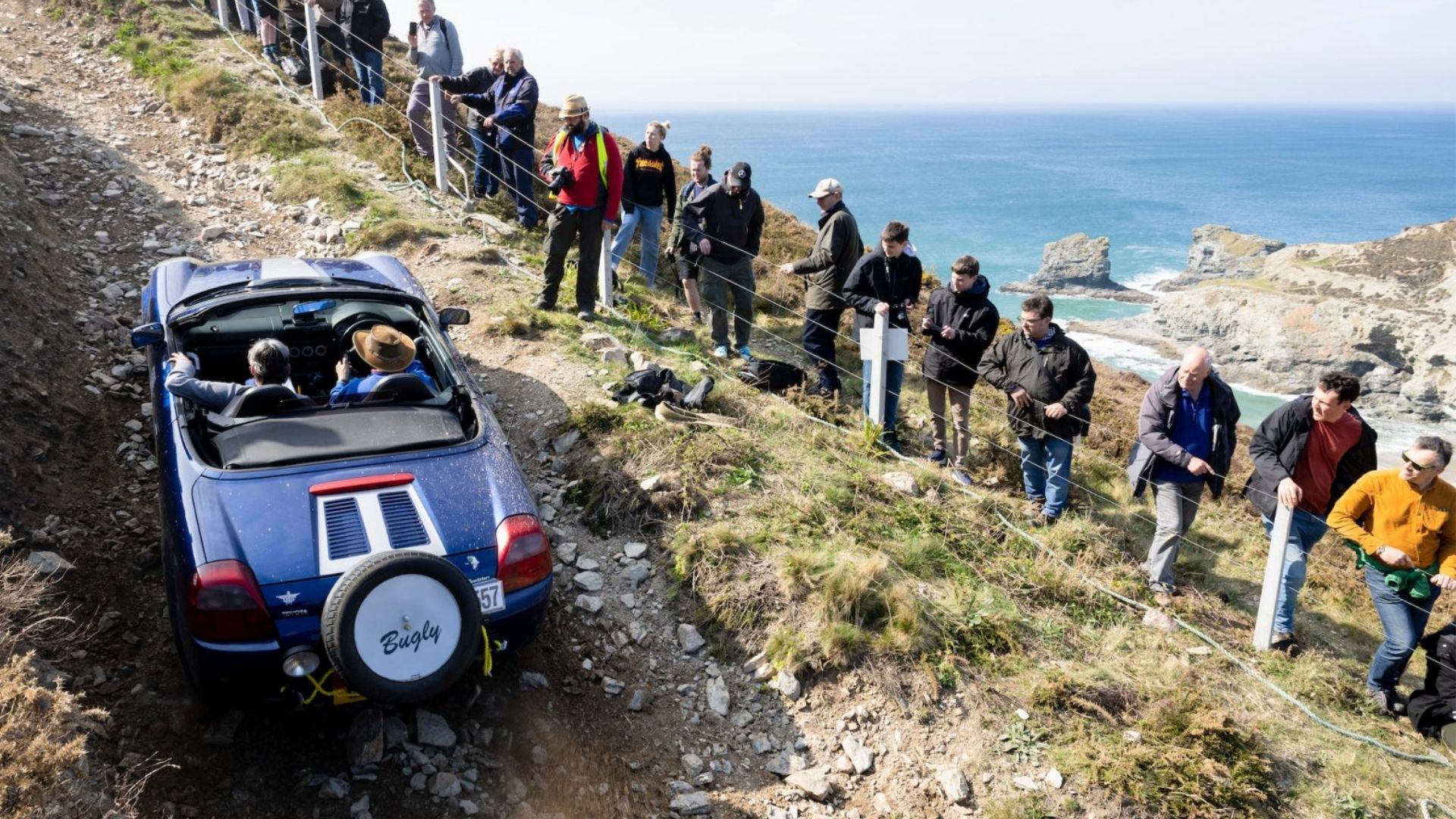 Blue car climbing rocky hill in a crowd