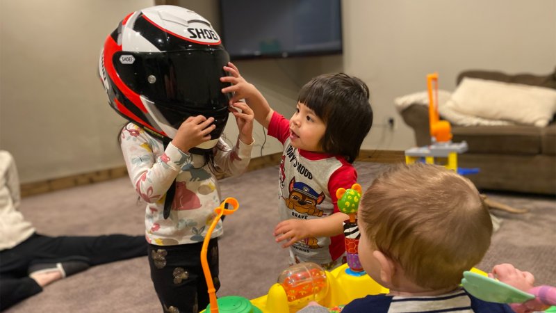 One child plays with a motorcycle helmet while two other children look on.