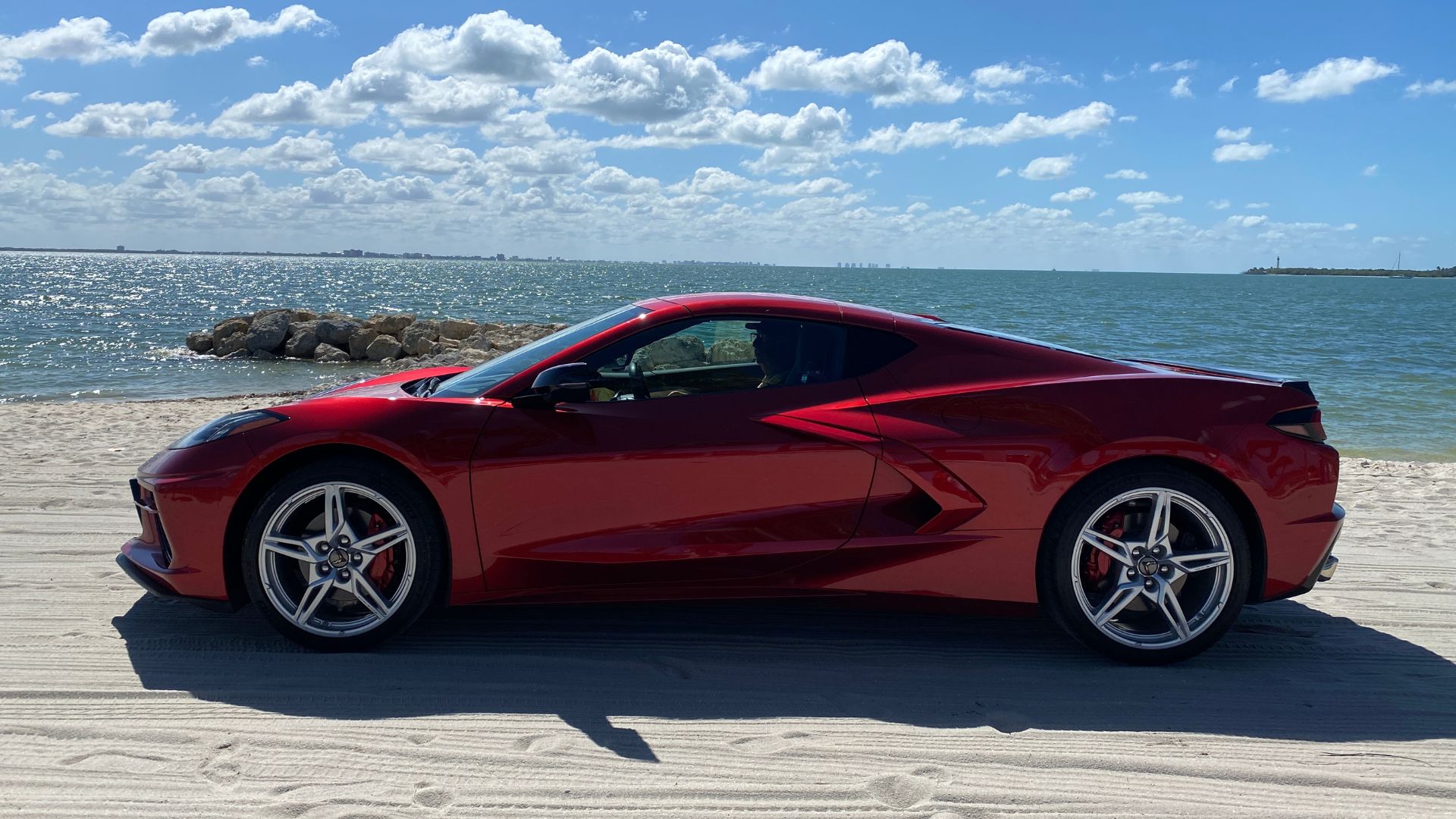 red Corvette on sandy beach with blue sky