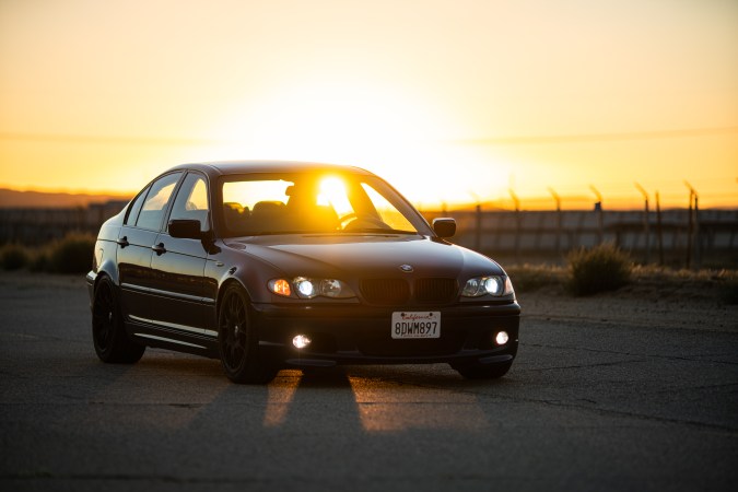 A blue BMW at sunset. The sun is piercing through its windows directly at the camera.