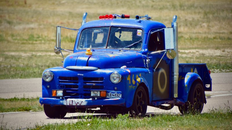 A blue 1950 Dodge pickup with exhaust stacks against a grassy backdrop