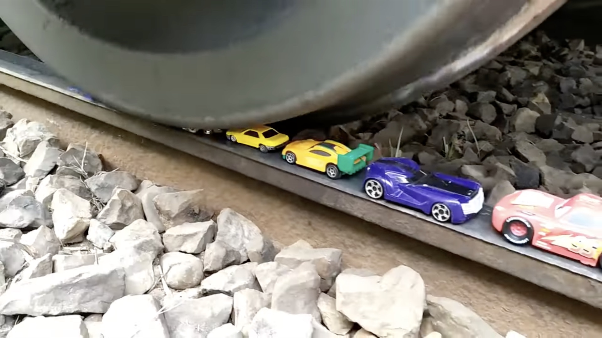 A train wheel crushes a series of toy cars left on the rail