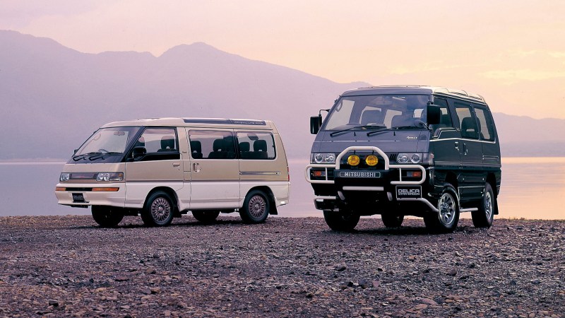 Mitsubishi Delicas on the shore of a lake with a mountain backdrop