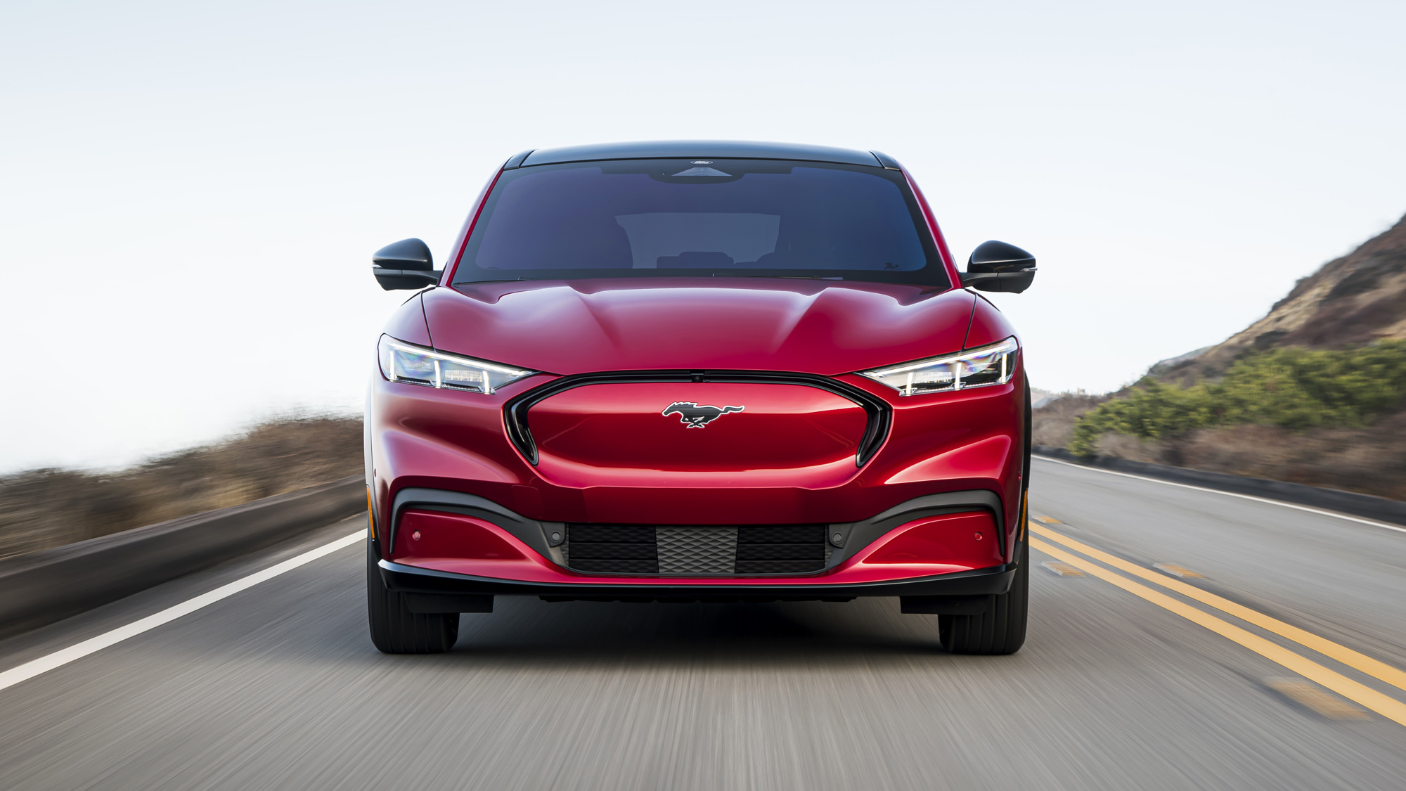 Front head-on image of a red Ford Mustang Mach-E at speed on a road.