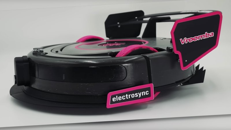 World's fastest Roomba robot vacuum cleaner. The Roomba has visible pink wheels and trim on its aerodynamic elements, including pink-rimmed front and rear wing end plates.