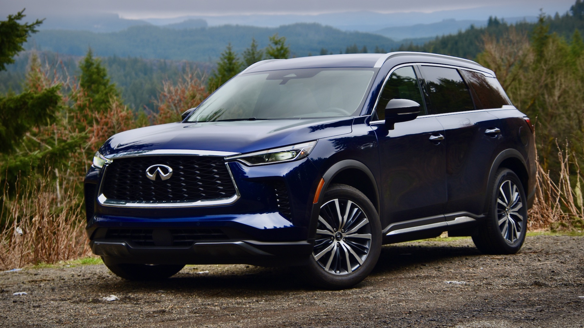 2023 Infiniti QX60 Sensory AWD in dark blue. The SUV is against a forested, mountainous background