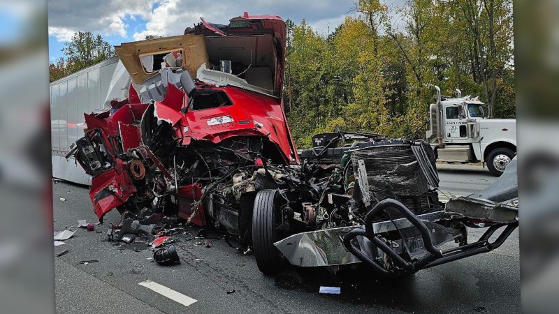 A heavily damaged red semi truck with the cab crushed and torn away