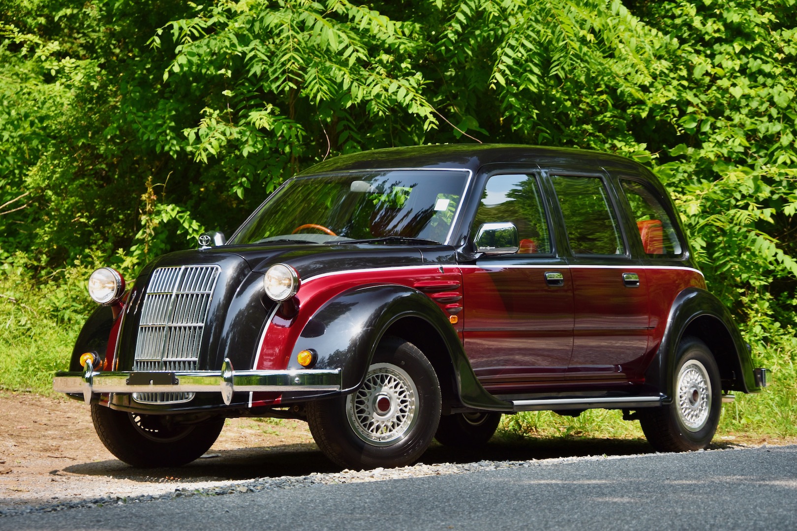 1996 Toyota Classic front three-quarter against a background of greenery. The car has a two-tone color scheme with red sides, a black roof and hood, and the two colors are separated by a thin white strip.