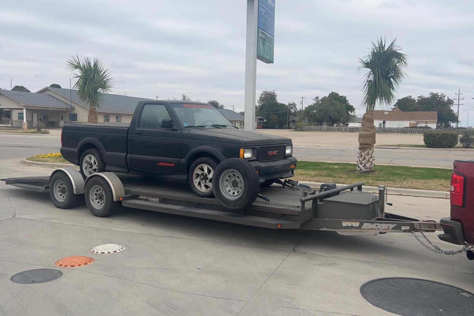 A GMC Syclone on a trailer in a tropical setting, with palm fronds visible by the side of the road