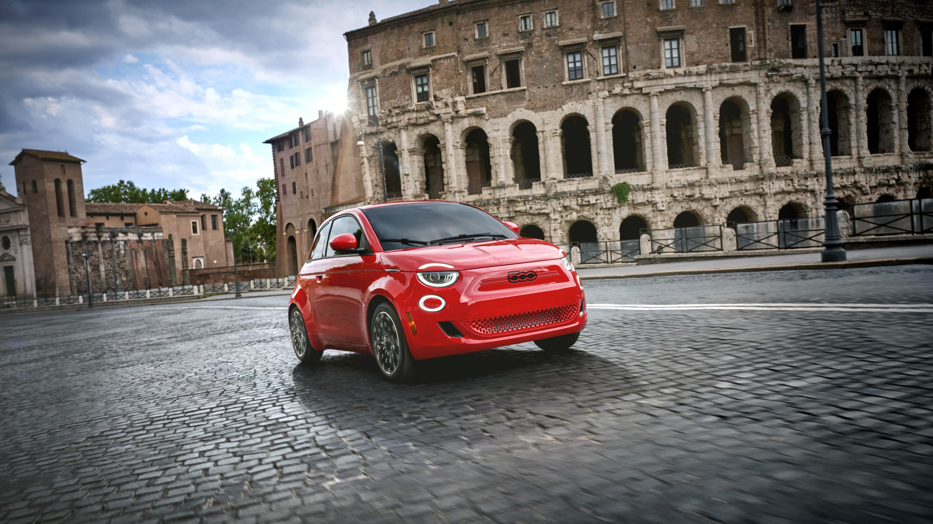 A red Fiat 500e driving on a cobblestone street.