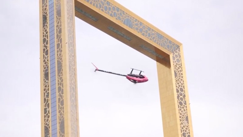 A remote-controlled helicopter flying upside down in front of a golden arch