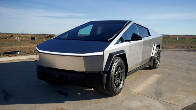 A front three-quarter view of a Tesla Cybertruck posed on concrete in the middle of a field.