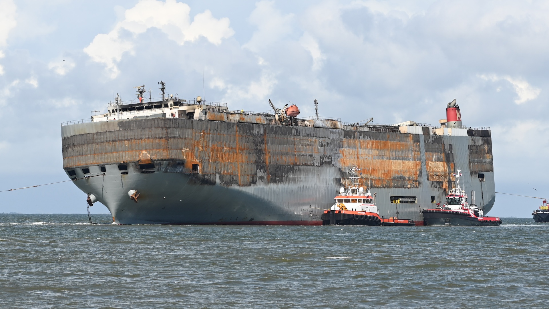 03 August 2023, Netherlands, Eemshaven: Tugs pull the badly damaged car carrier "Fremantle Highway" into the harbor. A good week after the fire broke out, the approximately 200-meter-long ship had been towed for hours to the North Sea port at the mouth of the Ems River. Photo: Lars Penning/dpa (Photo by Lars Penning/picture alliance via Getty Images)