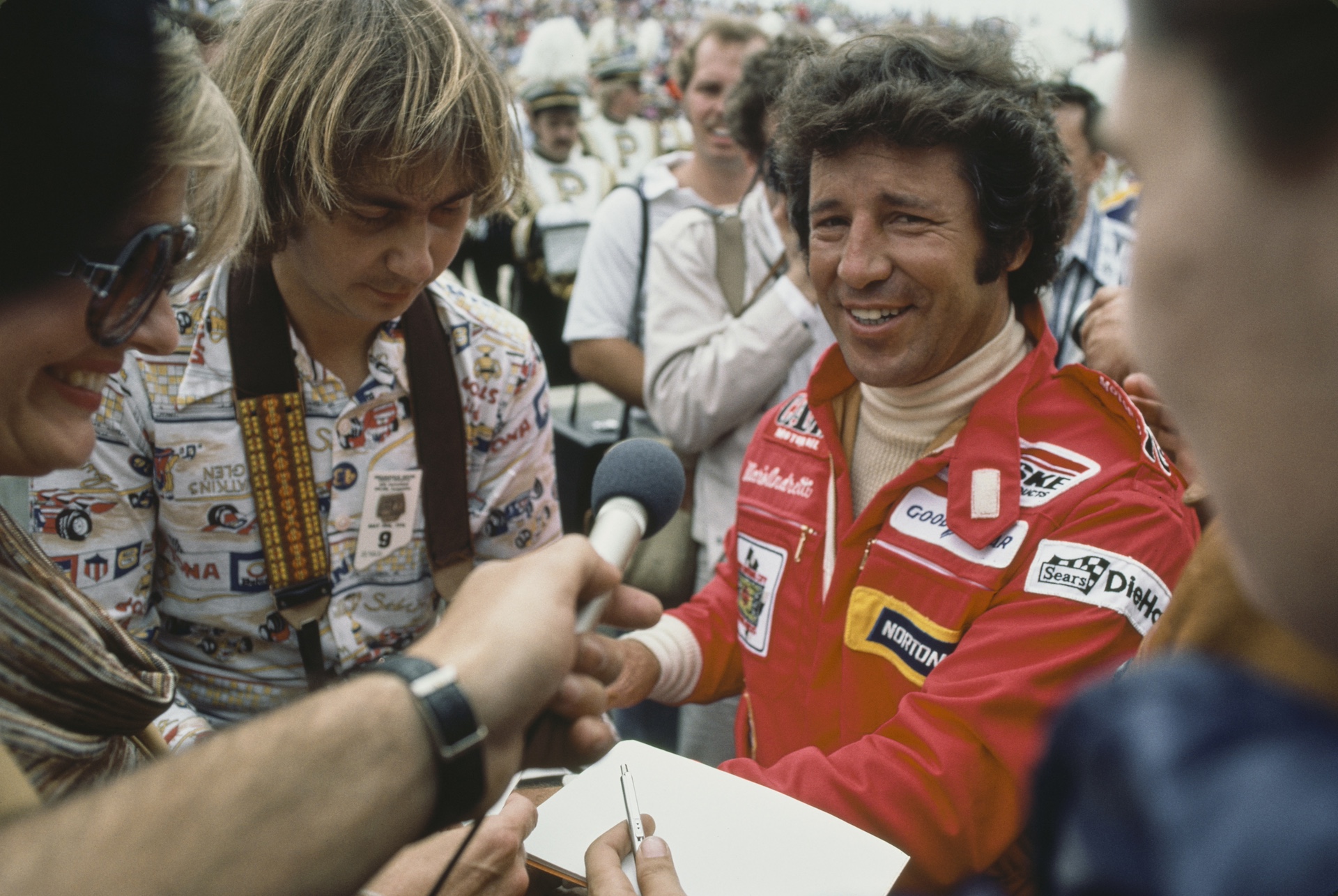 Italian-born American former racing driver Mario Andretti wearing coveralls interviewed as he signs autographs for fans at the 62nd 500-Mile International Sweepstakes (Indianapolis 500), staged at the Indianapolis Motor Speedway in Speedway, Indiana, 28th May 1978. (Photo by Michael Montfort/Michael Ochs Archives/Getty Images)