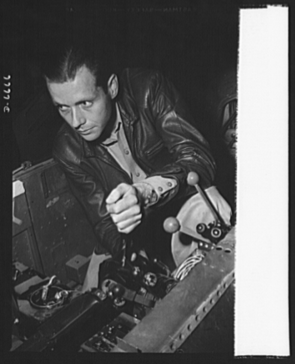 A factory worker tests gun controls in a Lockheed P-38 Lightning before delivery. Note the ball-topped throttle levers in the right side of the photo.