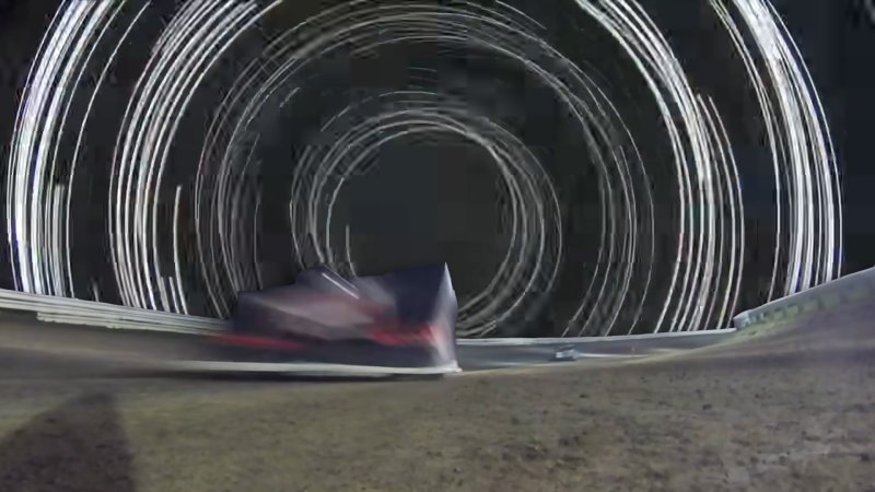 A dirt oval car approaches the camera as the background shows a swirl of light, superimposed from a later frame in the video.