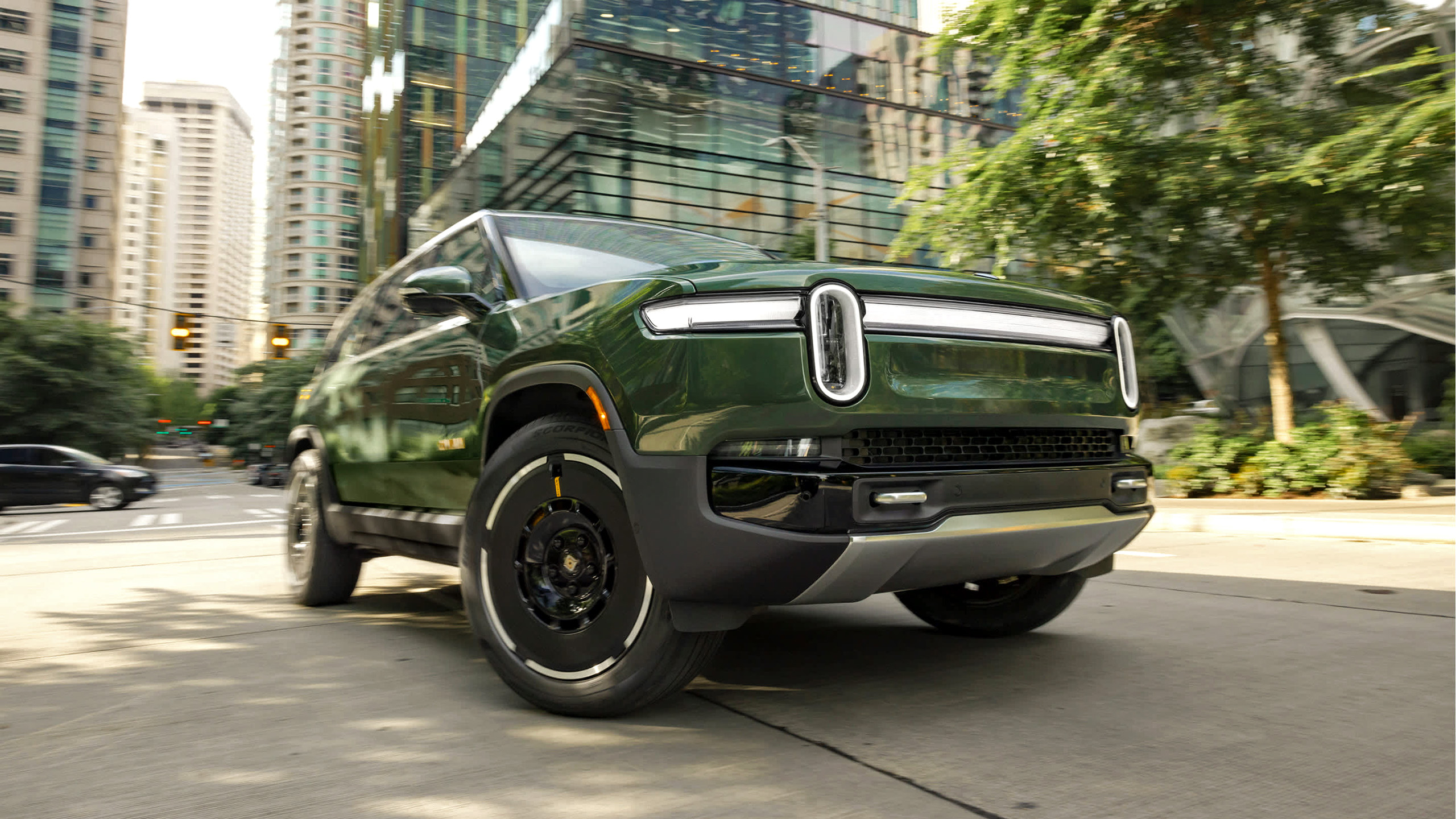 A green Rivian R1S driven in a city.