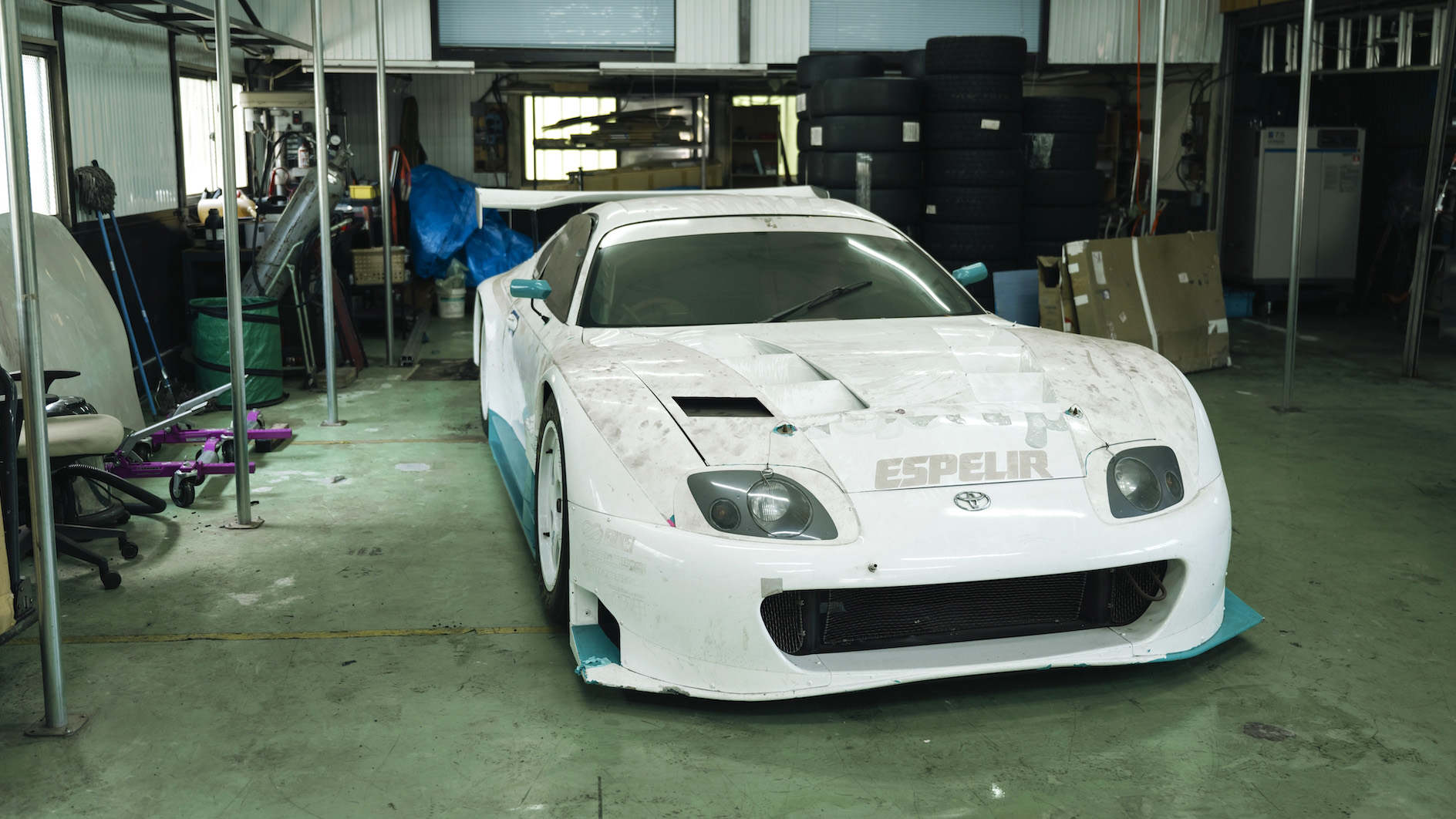 A 2000 JGTC Toyota Supra race car in a white livery in a garage in Japan.