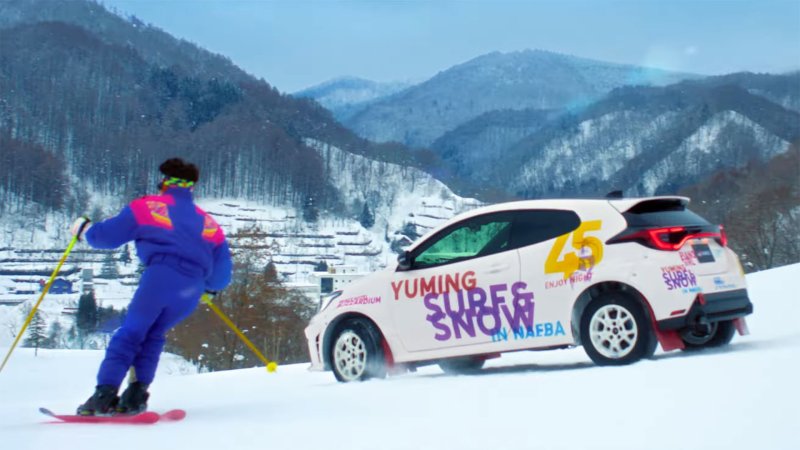 Screenshot of clip from Toyota Gazoo Racing music video with GR Yaris driving down mountain next to skier.