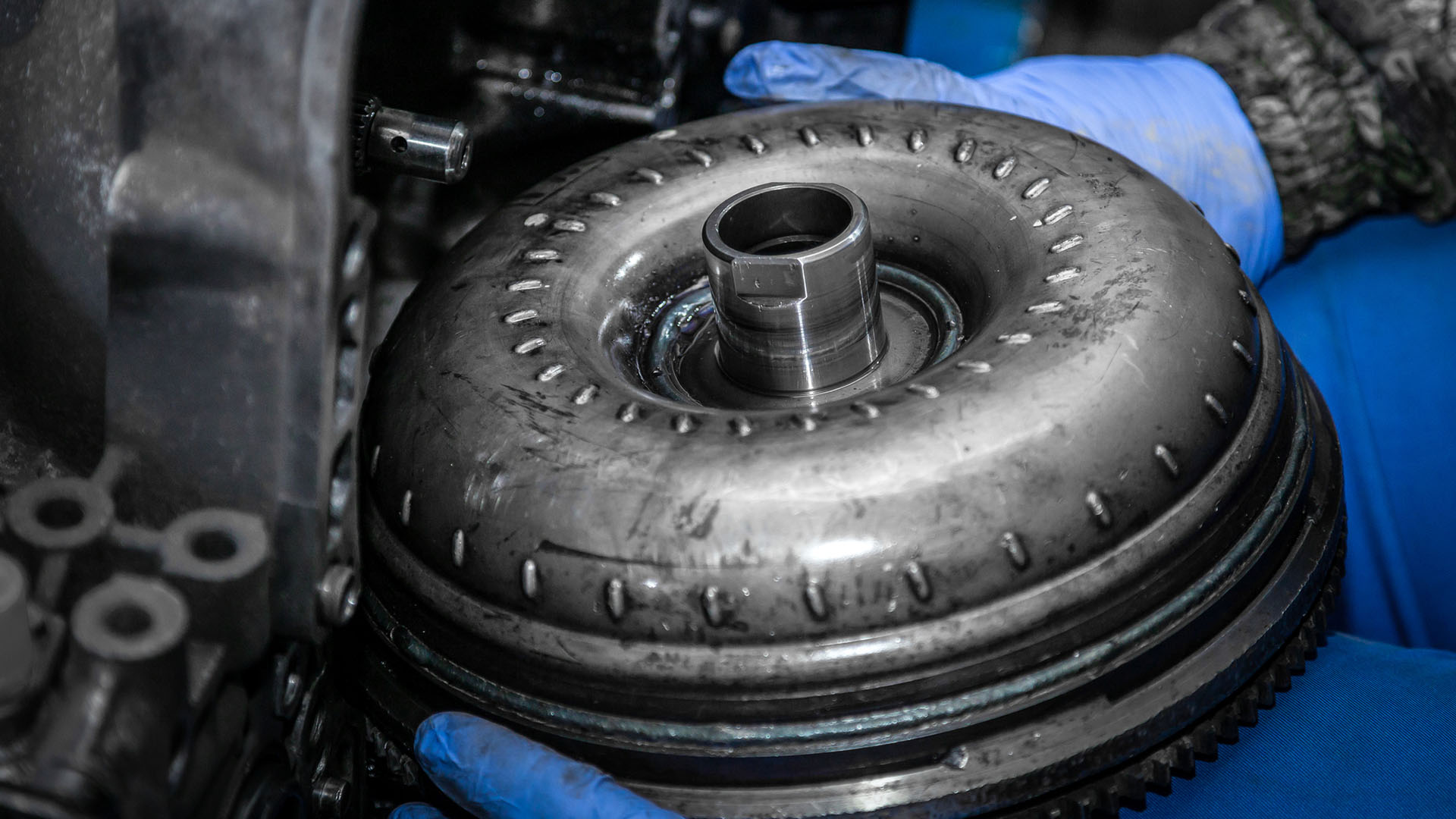 A mechanic removes a torque converter from the transmission.