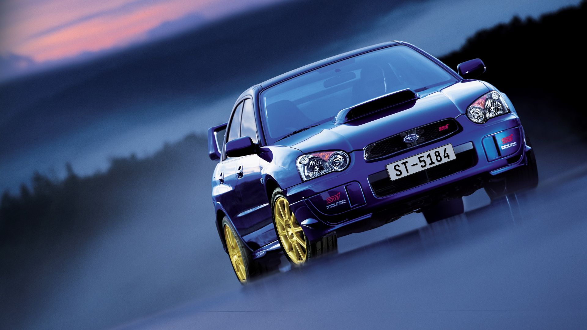 A blue Subaru WRX STI poses with gold wheels.