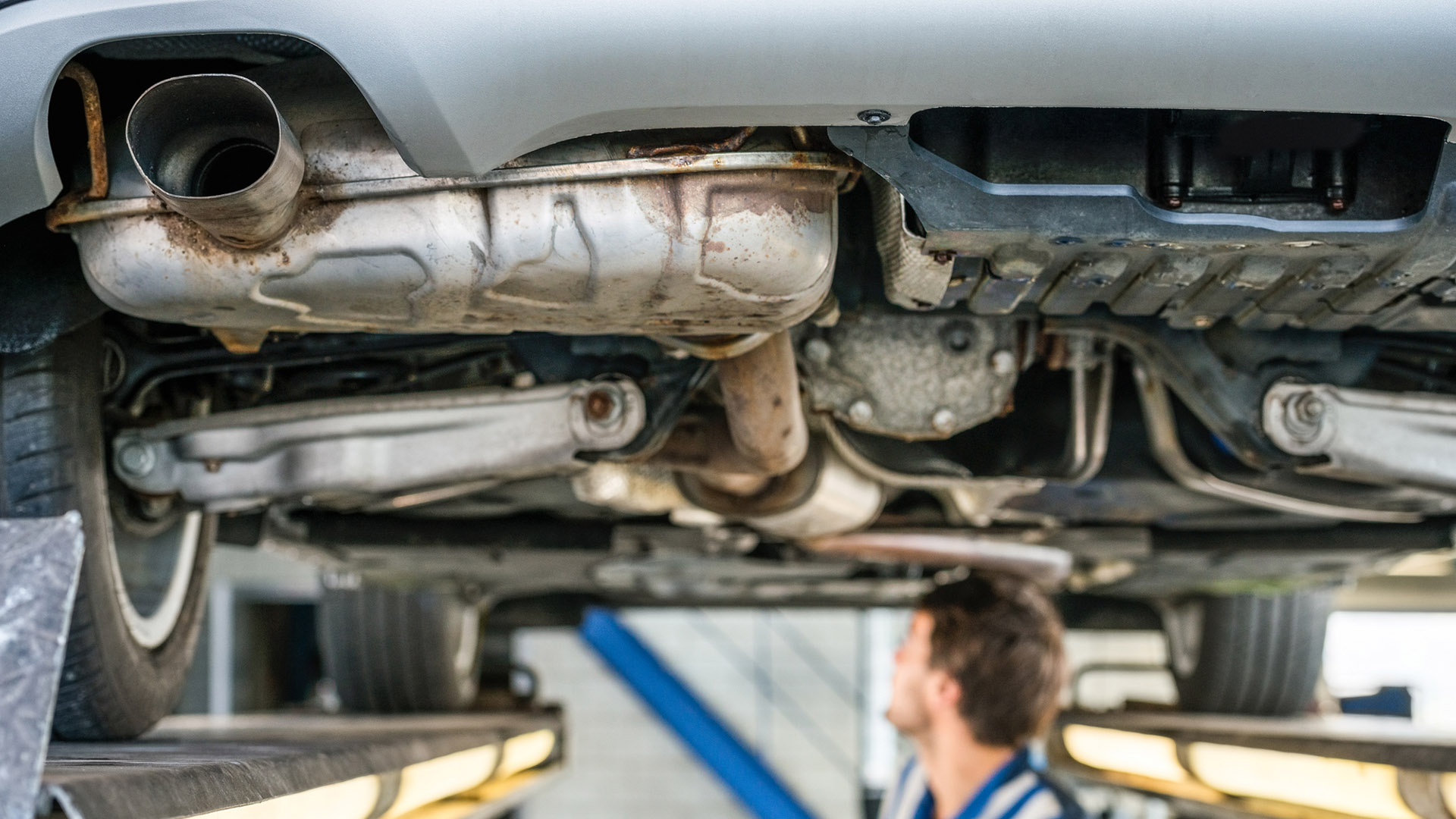 A mechanic looks at the underside of a car on a lift.