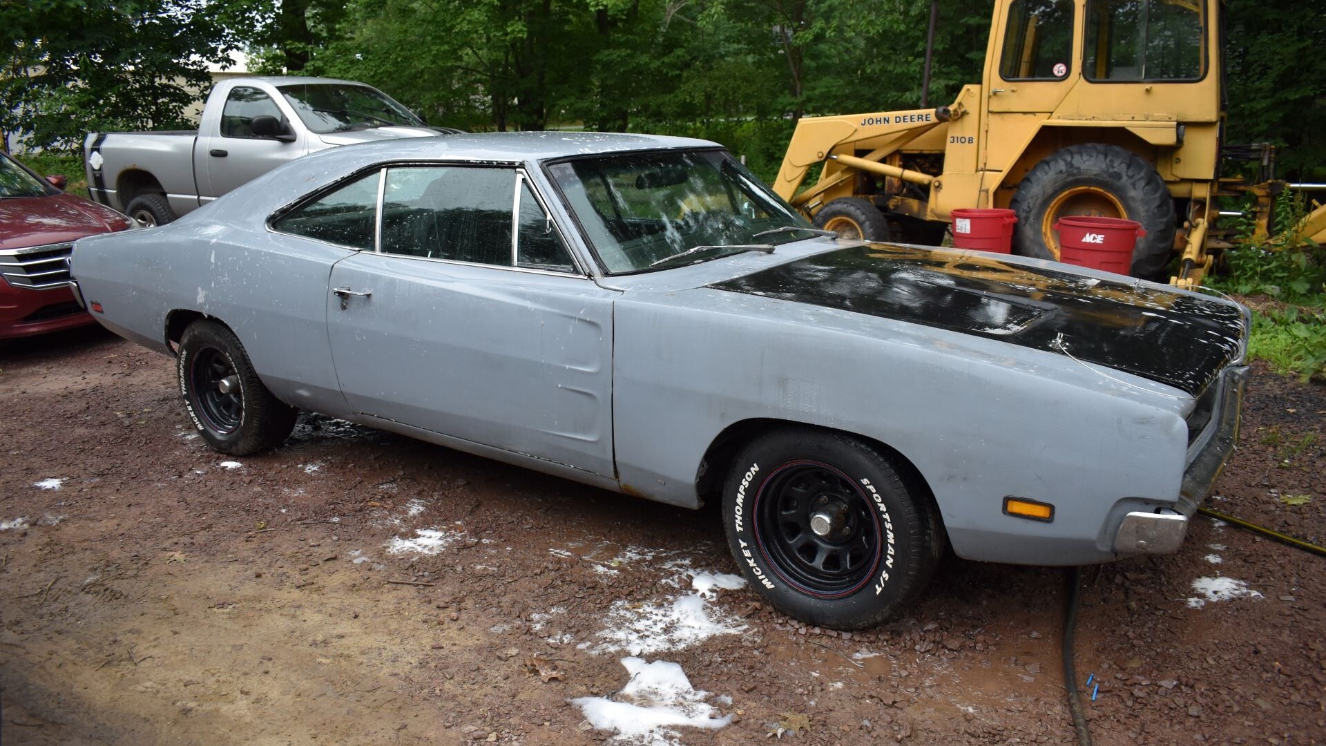 A gray and black classic Dodge Charger next to a bulldozer.