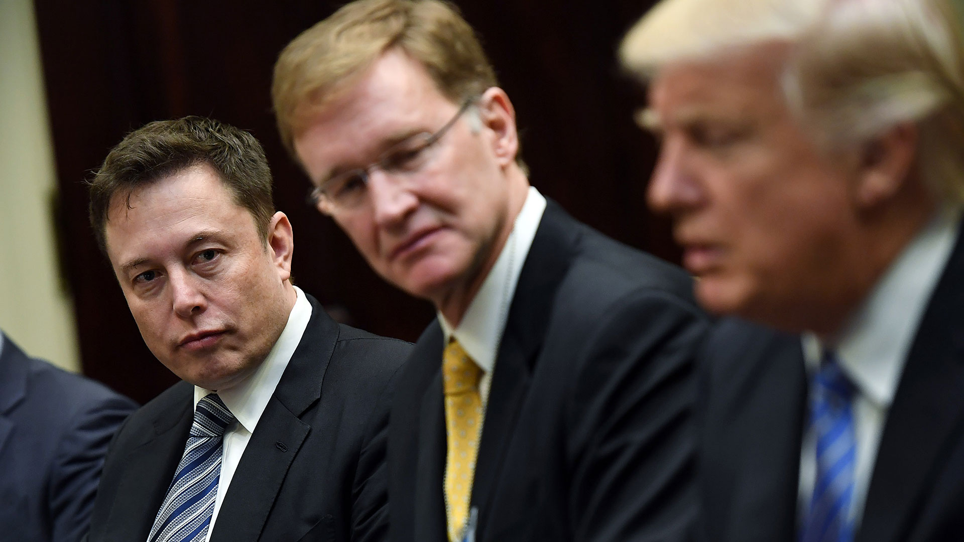 Elon Musk sits at a table looking over at President Donald Trump during a meeting with business leaders at the White House on Monday, January 23, 2017.